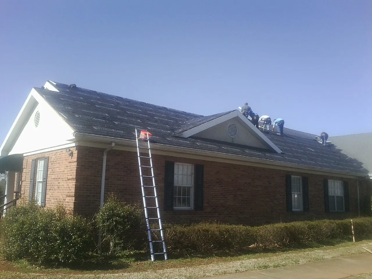 Crew tearing shingles off a brick ranch roof with a ladder set — Metal Roof Repair work by our crew in Oak Ridge